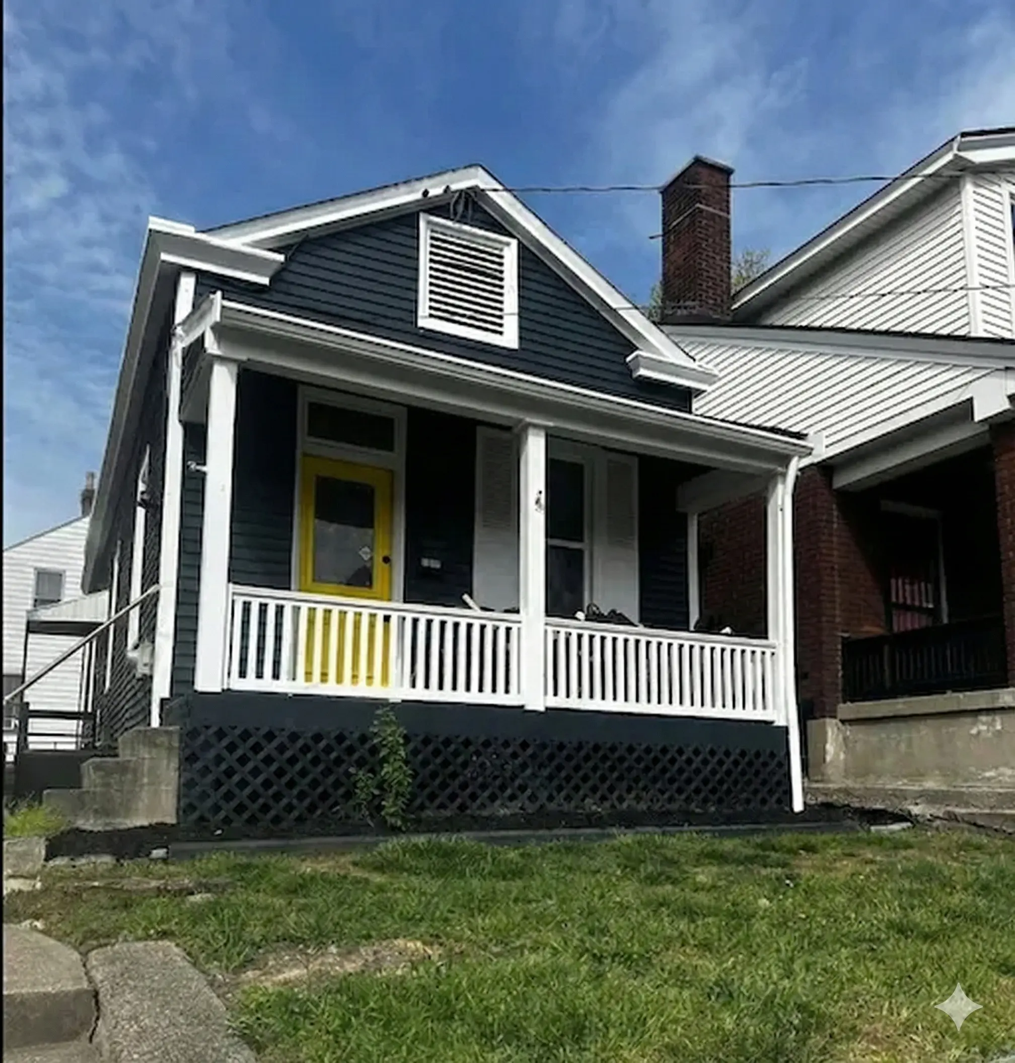 Exterior of a small dark grey cottage with white trim and a front porch.